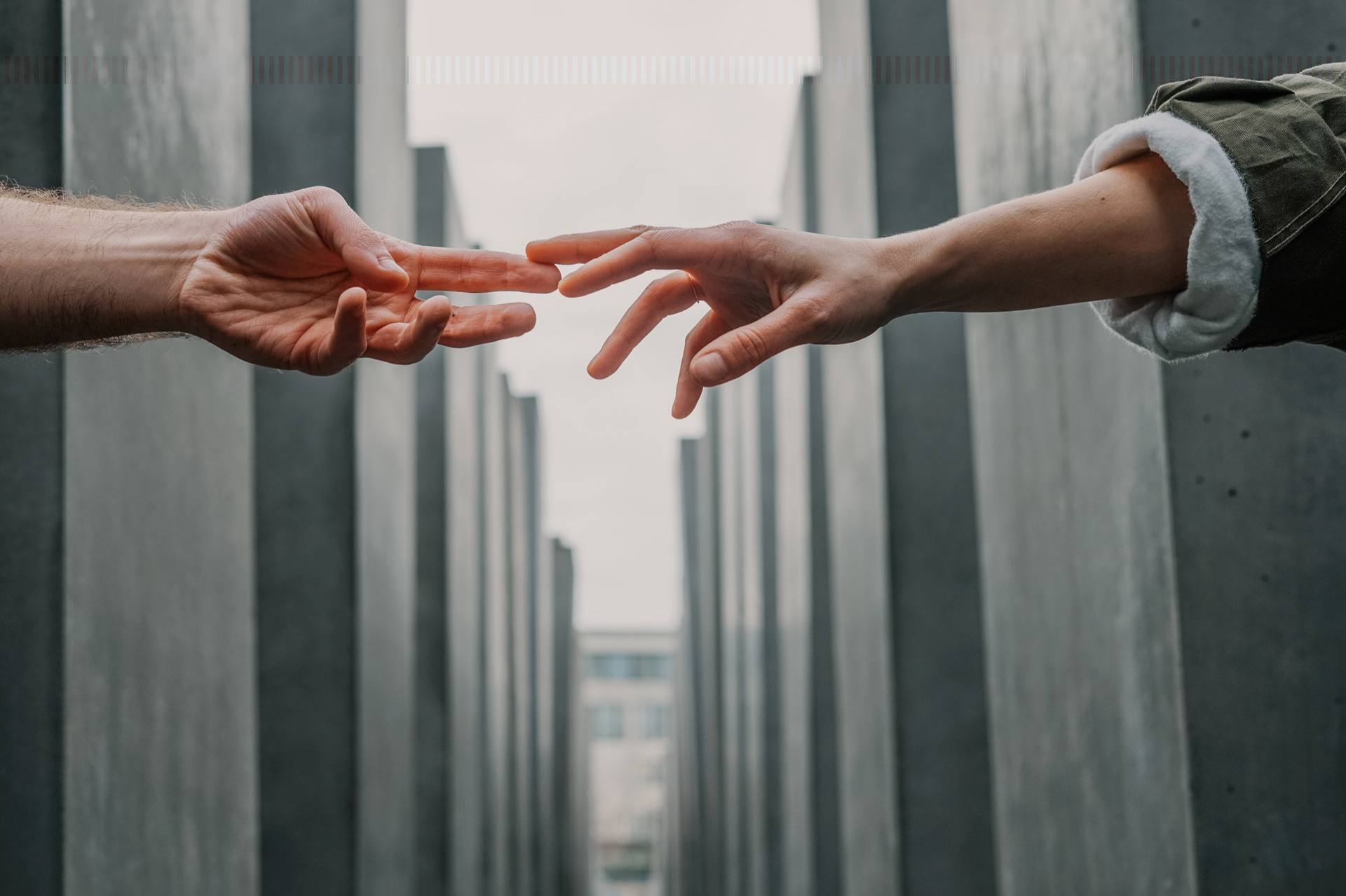 Two hands reaching toward each other between tall concrete columns, not quite touching