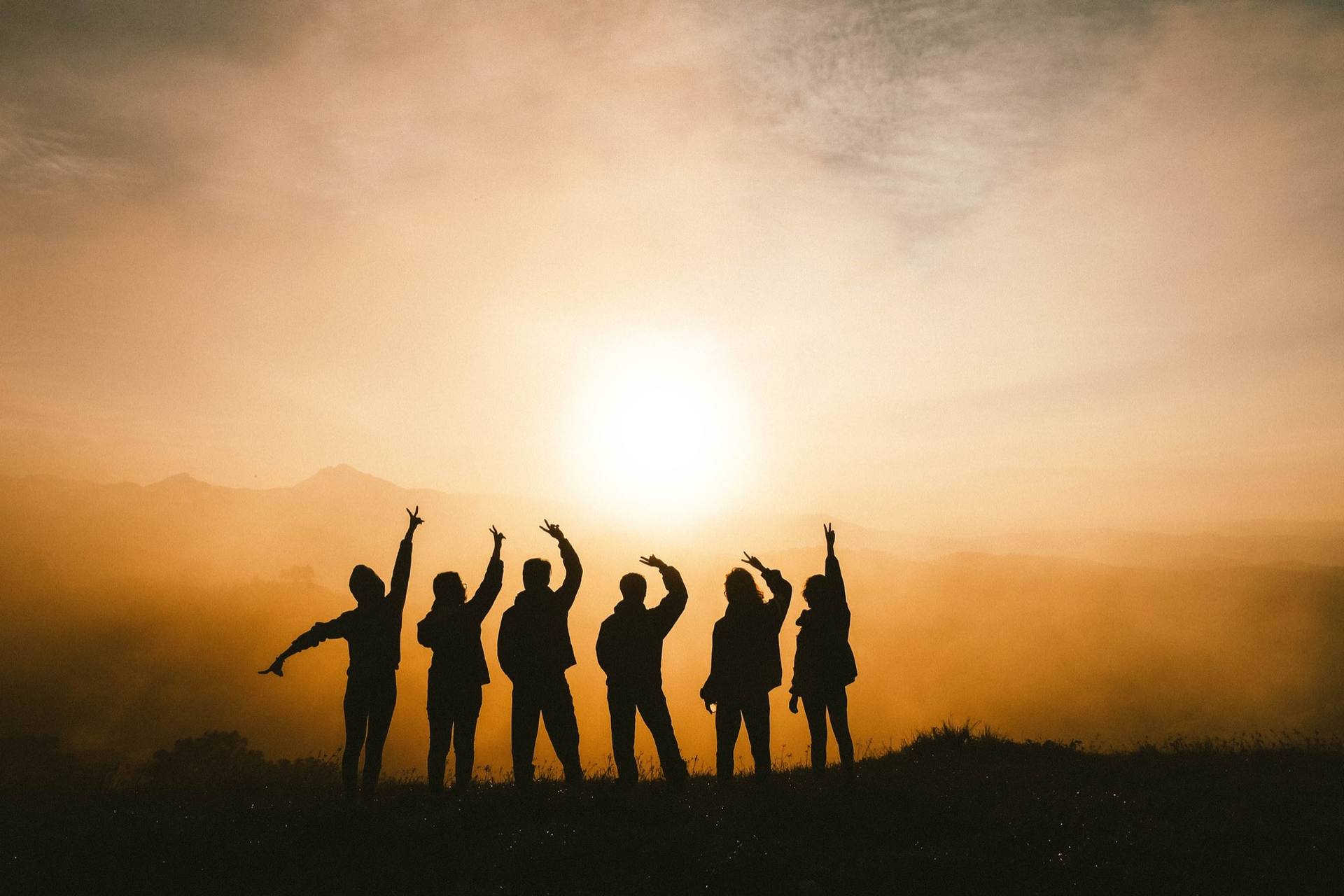 A team standing together on a ridge at dawn, arms raised toward the horizon